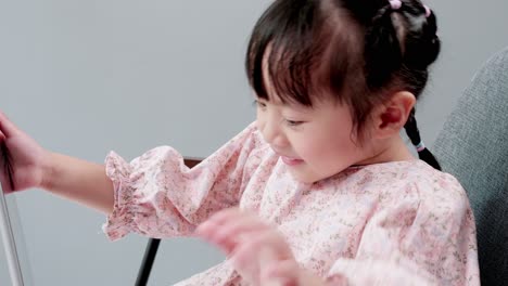 Kleines-Asiatisches-Mädchen-Sitzt-Auf-Einem-Stuhl-Und-Schaut-Sich-Online-Videos-Auf-Einem-Tablet-An-Und-Spielt-Videospiele