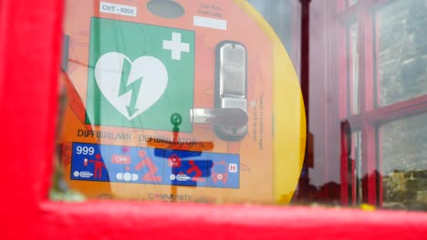 Medical-emergency-cardiology-defibrillator-device-in-old-red-British-public-village-phone-box-slow-left-dolly-shot