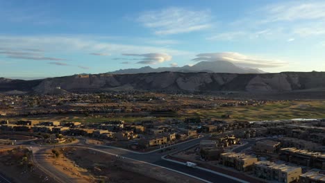 Panorama-Aéreo-Que-Revela-Casas-En-La-Ciudad-Sobre-Un-Fondo-De-Montañas-Y-Colinas-Al-Atardecer-Con-Cielo-Azul