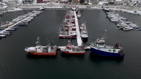 Flight-over-fishing-vessels-docked-at-Skjervoy-harbor,-Norway,-fresh-winter-snow