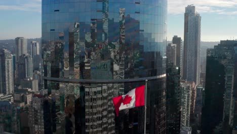 Bandera-Canadiense-Que-Sopla-En-El-Viento-Con-El-Exterior-De-Vidrio-De-Un-Edificio-Alto-En-Segundo-Plano-En-El-Centro-De-Vancouver,-Canadá