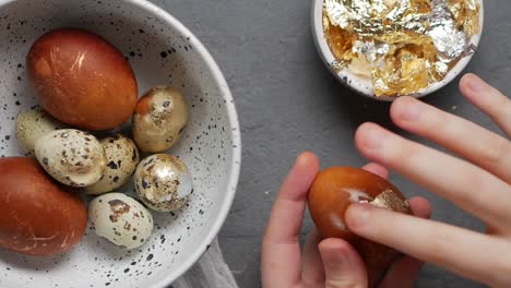 Close-up-shot-of-a-female-hand-ring-golden-foil-from-orange-colored-painted-Easter-egg