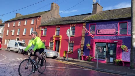 Un-Ciclista-Pasa-En-Un-Día-Soleado-Y-Ventoso-En-Ballinspittle,-Un-Pequeño-Pueblo-En-El-Condado-De-Cork,-Irlanda
