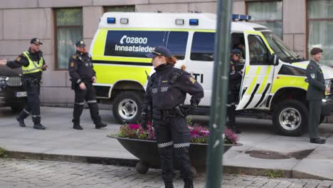 Mujer-Policía-De-Pie-En-Karl-Johan,-Oslo-Durante-El-Desfile-Militar-Con-Coche-De-Policía-Detrás