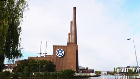 Vista-Mirando-El-Logotipo-De-VW-En-El-Lateral-Del-Edificio-De-La-Fábrica-De-Volkswagen-Con-Torres-De-Chimenea-En-Wolfsburg,-Alemania