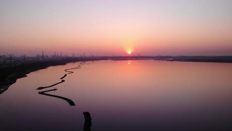 Aerial-Over-Calm-Waterway-With-Reflected-Orange-Sunset-Next-To-Silhouetted-View-of-Maasvlakte-Industrial-Port