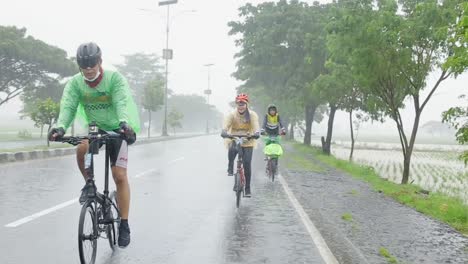 Male-athlete-cycling,-riding-bicycle-on-wet-road-in-rainy-day-wearing-helmet-and-raincoat