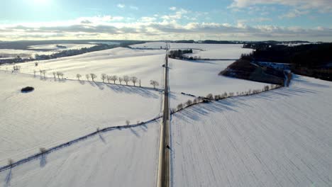 Aerial-view-of-a-road-leading-to-the-horizon-with-moving-cars-in-a-snowy-landscape