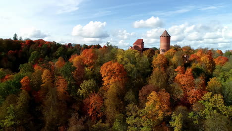 Aerial-forwarding-shot-over-a-medieval-Turaida-Castle,-Sigulda-in-the-Vidzeme-region-of-Latvia-surrounded-with-colorful-autumnal-forest-at-sunset