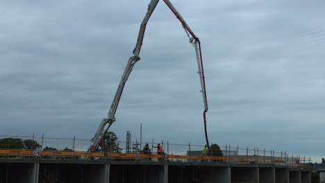 Pouring-of-concrete-floors-with-crane-moving-around-and-dispersing-building-material-where-needed-at-PUUR12-construction-site-against-an-overcast-sky-with-clouds-forming-and-passing