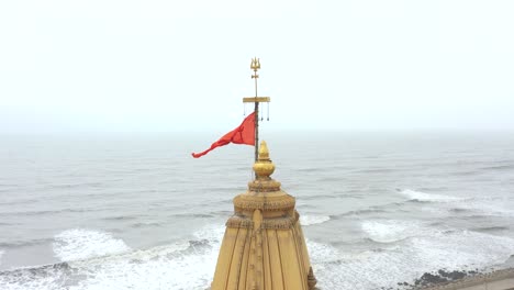 Toma-Aérea-Hacia-Atrás-De-La-Bandera-Hindú-De-Color-Azafrán-Que-Ondea-Sobre-El-Templo-Somnath-Ubicado-En-Prabhas-Patan,-Veraval-En-Gujarat,-India