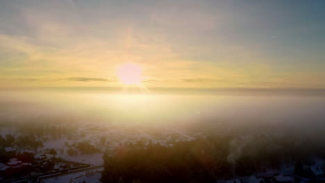 Filmischer-Luftflug-Durch-Dichte-Wolken,-Der-An-Einem-Verschneiten-Wintertag-Einen-Mystischen-Sonnenuntergang-Im-Hintergrund-Zeigt