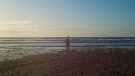 Pescador-Con-Una-Caña-De-Pescar-En-La-Orilla-Del-Mar-Al-Atardecer-En-La-Bahía-De-Holywell,-Cornualles,-Inglaterra---Tiro-Estático