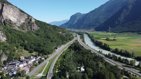 drone-view-through-the-valley-in-Valais-with-a-motorway,-a-motorway,-the-river-"Rhone"-and-a-small-village