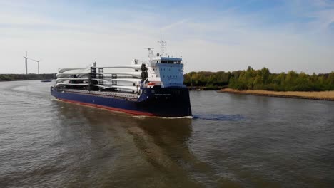 Drone-Shot-Of-Forward-Bow-Of-Symphony-Provider-Cargo-Ship-Transporting-Transporting-Wind-Turbine-Propeller-Blades-Along-Oude-Maas