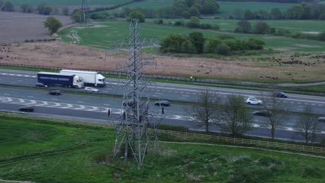 Speeding-traffic-passing-pylon-electricity-tower-on-M62-motorway-aerial-view-right-orbit-shot