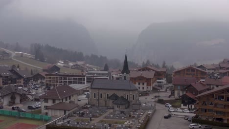 Aerial-of-Saint-Jean-de-Sixt-church-in-French-Alps,-scenery-of-recreational-village-with-wooden-buildings-in-mountains