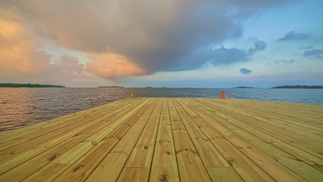 Close-up-view-of-old-wooden-jettie-by-a-lake-with-white-cloud-movement-in-timelapse-in-the-evening-time