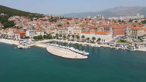 Aerial-drone-forwarding-shot-showing-ancient-roman-town-beside-blue-sea-and-mountains-iin-the-background-in-Split,-Croatia-on-a-bright-sunny-day