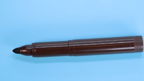 Brauner-Markierungsstift,-Der-über-Blauem-Oberflächenhintergrund-Rotiert,-Makroaufnahme,-Nahaufnahme,-Detailansicht