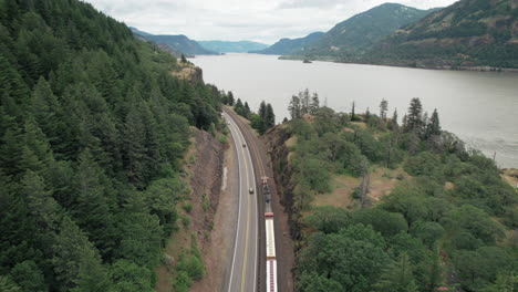 Aerial-dolly-forward-following-freight-train,-highway-traffic-along-Columbia-River