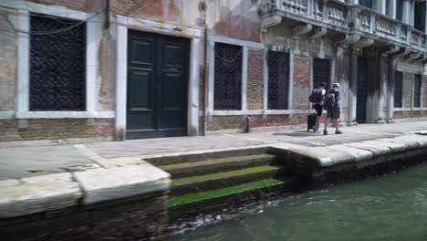 Gente-Caminando-Por-La-Orilla-Del-Canal-Desde-Un-Velero-En-Venecia,-Italia