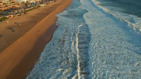 Aerial-view-above-ocean-waves-tilting-up-to-Reñaca-beach-Vina-Del-Mar-coastal-hotel-resort-buildings