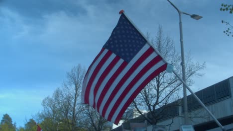 Flag-of-USA,-stars-and-stripes,-flies-diagonally-in-sunny-spring-park