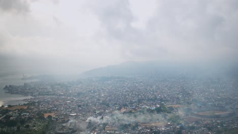 Aerial-hyperlapse-going-backwards-over-downtown-of-Freetown-Sierra-Leone-during-the-day-with-landfill-trash-burning