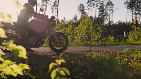Motorbiker-stopping-on-forest-roadside-on-warm-sunny-evening,-handheld-view