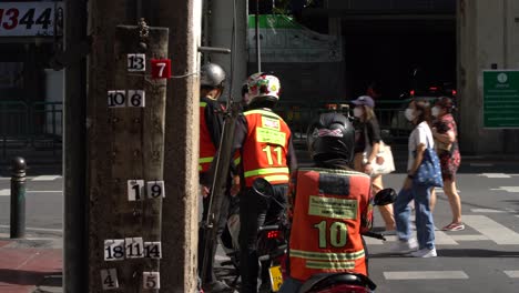 Thailändische-Motorradtaxifahrer-Tragen-Orangefarbene-Warnwesten-Und-Warten-Auf-Kunden-Auf-Saladaeng-Und-Silom,-Bangkok