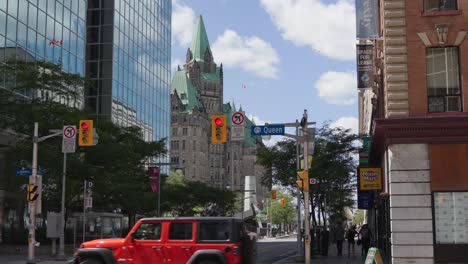 Vehicle-traffic-and-pedestrians-on-the-corner-of-Bank-Street-and-Queen-Street-in-downtown-Ottawa-before-Canada-Day-2022-with-the-Confederation-Building-in-the-background