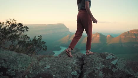 Woman-is-walking-towards-the-edge-of-a-cliff-to-enjoy-the-view-of-a-valley-during-sunset