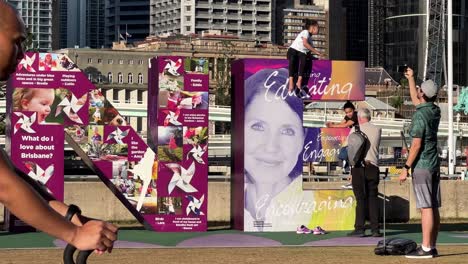 Family-taking-photos-with-giant-colorful-block-letter-of-Brisbane,-people-strolling-pass-the-iconic-landmark-at-downtown-river-bank-on-a-sunny-afternoon,-Queensland-the-sunshine-state,-close-up-shot