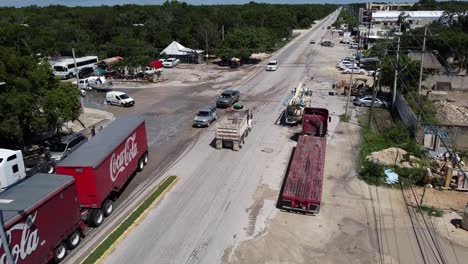 Coca-Cola-Semi-Truck-turning-onto-a-highway-road-in-Tulum-Mexico-on-a-sunny-day,-aerial