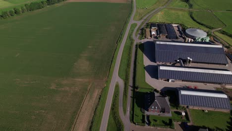 Large-farm-with-solar-panels-in-Dutch-river-valley-landscape-seen-from-above-following-the-embankment-with-a-road-on-top-meandering-through-the-agrarian-rural-area-near-Zutphen,-Netherlands