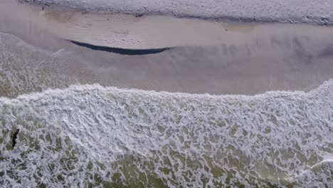 Aerial-footage-looking-straight-down-at-waves-rolling-onto-a-sand-beach