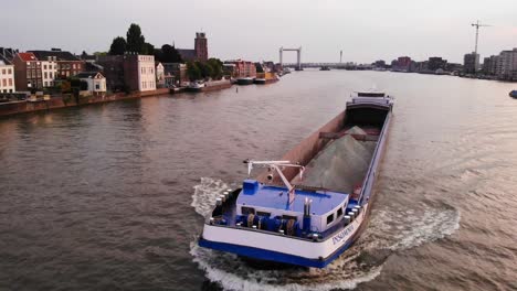 Luftdrohnenaufnahme-über-Einem-Frachtschiff-Mit-Schlaflosigkeit,-Das-Sich-Mit-Blick-Auf-Die-Brücke-Von-Moerdijk-Im-Hintergrund-In-Den-Niederlanden-Während-Der-Abendzeit-Bewegt