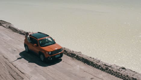 Orange-Jeep-Renegade-Longitude-cruising-on-off-road-journey-with-tourists,-aerial-view