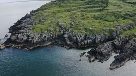 Flying-around-the-rocky-coastline-of-Clogherhead-with-the-calm-blue-ocean-on-a-sunny-day,-Ireland