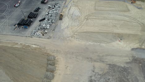 Aerial-view-of-a-Contruction-site,-trackers-and-Bolders-are-standing-along-with-a-crossroad-and-car-parking-near-by