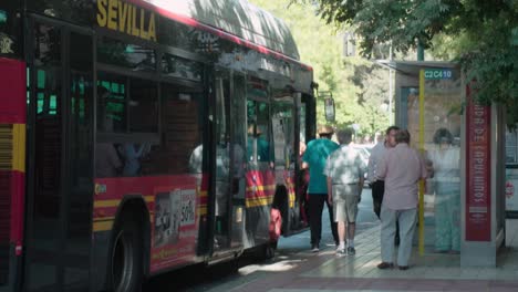 People-getting-onto-red-bus-that-drives-away-in-Seville,-Spain