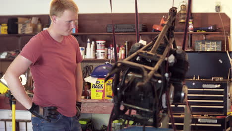 Medium-Shot-of-Young-Blonde-Man-Gauging-Progress-During-Motorcycle-Teardown