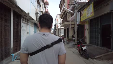 View-of-the-back-of-a-man-while-walking-in-local-suburb-road-street-area-in-Phuket,Thailand