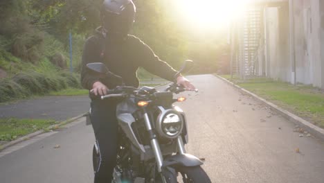 Motorradfahrer-Mit-Helm-Setzt-Sich-Auf-Sein-Motorrad-Und-Startet-Bei-Sonnenuntergang-Eine-Fahrt