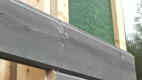 Worker-Tightens-The-Screw-With-A-Screwdriver-In-Wooden-board,-working-on-exterior-facade-of-a-new-house,-static-closeup-shot-in-slow-motion