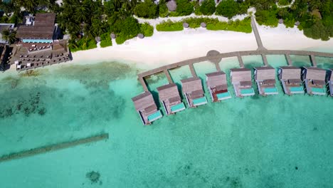 Die-Schönen-Und-Ruhigen-Bungalows-über-Dem-Wasser-Eines-Resorts-Auf-Tahiti-Mit-Sauberem,-Kristallklarem-Wasser-Und-Weißem-Sandstrand-–-Luftaufnahme