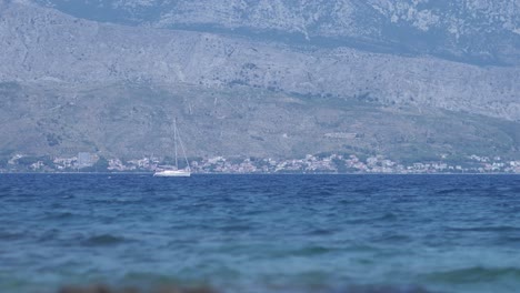 White-sailboat-navigates-off-the-coast-of-Postira,-Island-of-Brac---Croatia-travelling-from-left-to-right-of-the-frame