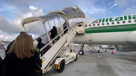 Passengers-board-Alitalia-Ari-Airplane-via-staircase-from-airport-Tarmac,-hand-held
