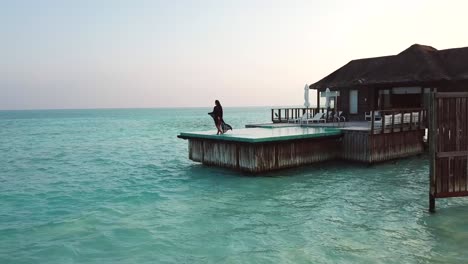 Luftaufnahme,-Zeitlupe,-Drohnenaufnahme,-Eines-Mädchens,-Das-An-Einem-Sonnigen-Tag-Auf-Der-Insel-Conrad-Rangali-Auf-Den-Malediven-Auf-Dem-Pool-Des-Sonnendecks-In-Einer-Villa-Am-Meer-Spaziert